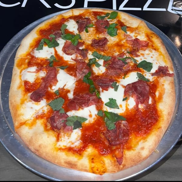 Jack's Pizza: a whole pizza with red sauce, fresh mozzarella, prosciutto, and basil on a metal pan.