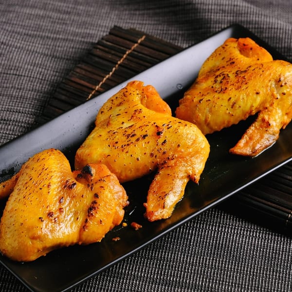 Three golden-brown baked chicken wings seasoned with spices, served on a black rectangular plate.