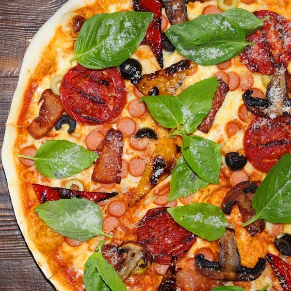 Close-up of a Jack's Pizza with basil, tomatoes, sausage, mushrooms, and olives.